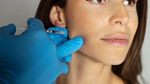A physician injecting botox in the masseter muscle of a woman.