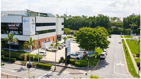 Aerial image of a two-storey building complex, street and many cars parked in front of it.