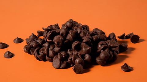A pile of chocolate chips spread on an orange surface.