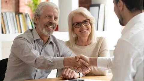 An elderly couple is discussing something with a young person and shaking hands with him.