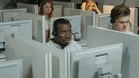 A group of call center employees wearing headsets are seated in a cubicle space, working on their computers.