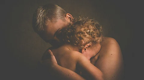 A woman embraces a child in a dimly lit room.