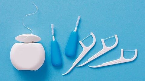 Hand floss, interdental brush and a string floss all placed on a blue surface.