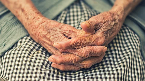 An elderly woman's hands are gently folded on her lap, showcasing her delicate skin and silver rings.