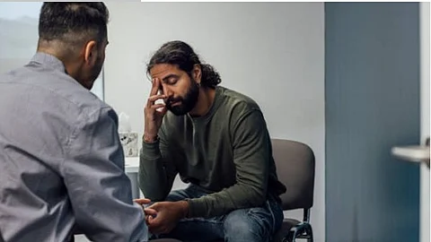 A person is looking distressed while talking to another man in a room.