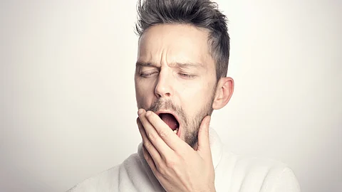 A man in a bathrobe yawns, appearing relaxed and sleepy in a cozy setting.