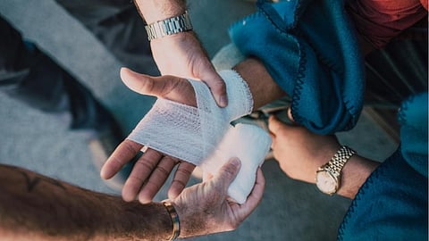 A patient is helping to tie up a gauze on another person's hand.