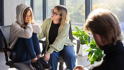 Teen girl and mom at therapy with therapist taking notes.