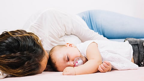 An infant and mother sleeping on a white bed.