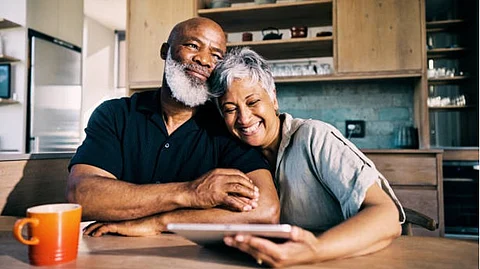 An old couple watching something in a tab with a smile holding each other.