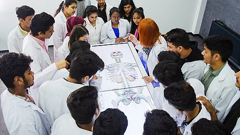 A group of students in lab coats examines a skeleton, engaged in a learning activity in a laboratory setting.