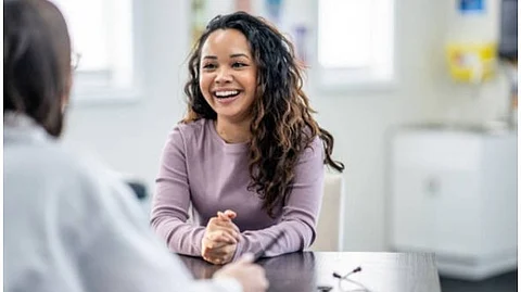 A woman smiling at another person sitting at a table across her in between a conversation.