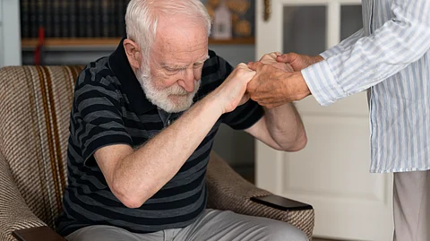 An old man being helped to get up from the chair.