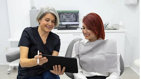 A female doctor in black scrubs is explaining something to a female patient in a tab inside a clinic.