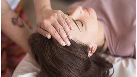 A person is holding a woman's head in their hands while the woman is lying down with her eyes closed.