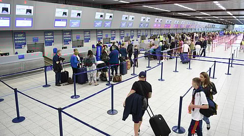 A line of travelers waiting at an airport check-in area, with luggage and boarding passes in hand.