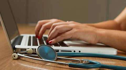 A person using a laptop and a stethoscope nearby.