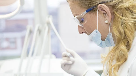 A female doctor wearing blue surgical mask, goggles, gloves is using a scaling instrument.