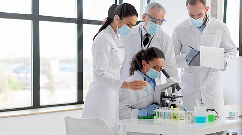 A group of people in lab coats examining a sample in a pharmaceutical company laboratory setting.
