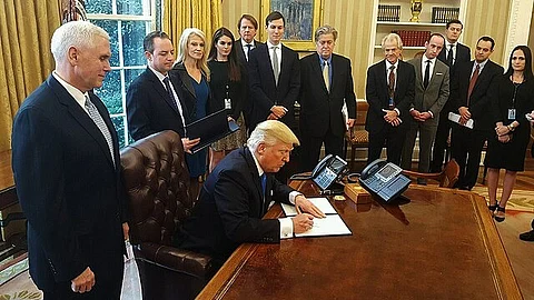 President Donald Trump is signing some documents while many people are standing around him.