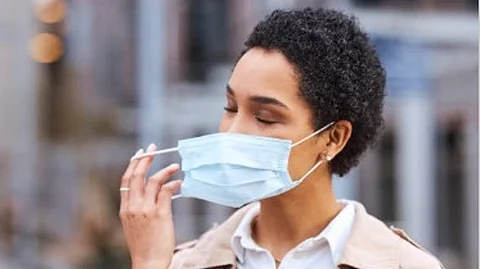 An image of a woman taking off a surgical mask.