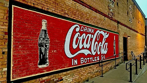 A large red and white Coca-Cola sign prominently displayed on a brick building.