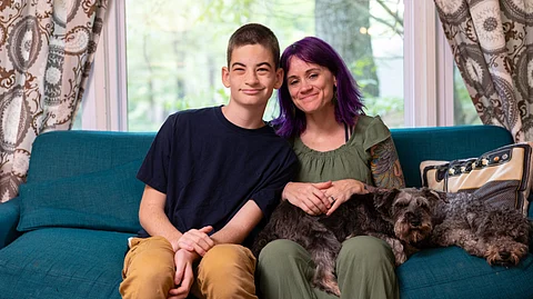An image of Ali Shenk and her son sitting on a teal-colored sofa inside their home.