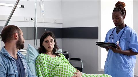 A pregnant couple is receiving medical advice from a nurse in a hospital ward.