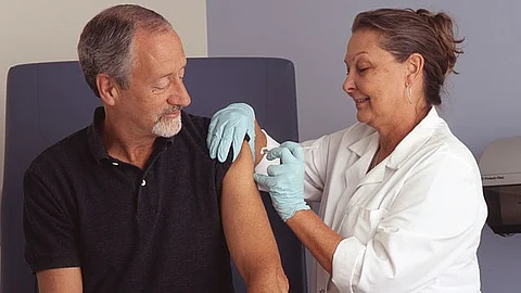 Nurse in white coat with a syringe containing vaccine injected in the arm of an older adult male.
