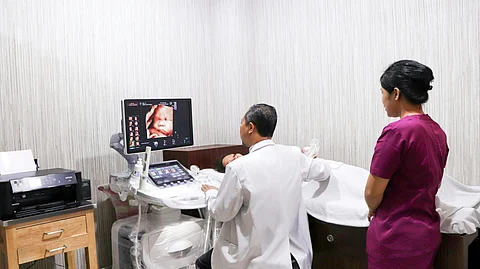 A pregnant woman is being examined by a doctor while a nurse is standing nearby.