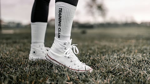 A person stands in grass, wearing white socks, demonstrating efficient lower limb movement for optimal energy use.