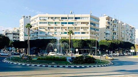 A street scene featuring a traffic light with a building representing a hospital visible in the background.