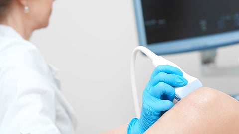 patient is undergoing ultrasound of leg with white color ultrasonic tool on the knee