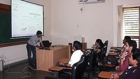 A man stands before a group, giving a presentation while the audience listens intently in a meeting room.