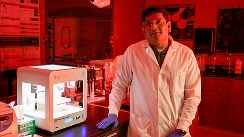 A man wearing white apron and surgical gloves, and standing in a research lab.