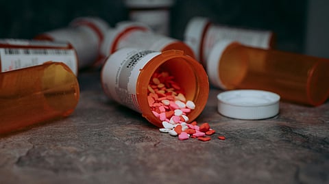 A prescription bottle tipped over with colorful pills spilling out onto a white surface.
