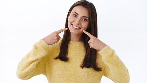 A woman smiling and pointing at her healthy mouth with both index fingers.