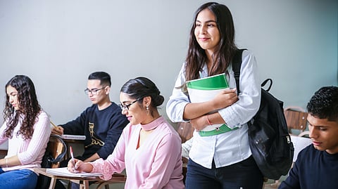A woman stands in front of a group of students, actively engaging them in a learning environment.