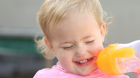 The image shows a child chewing a plastic feeding bottle.
