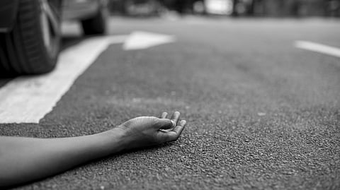 A woman is lying lifelessly on a road with a car parked beside her.