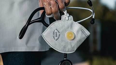A healthcare professional with a mask and stethoscope stands prepared for a medical examination.