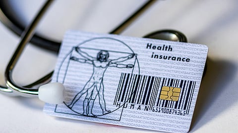 A health insurance card is placed along with a stethoscope on a white table.