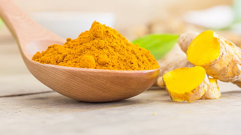 The image shows a spoonfull of turmeric.
