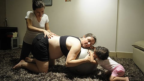 A Doula is supporting a pregnant woman on birthing ball.