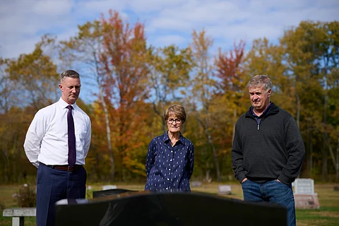 Two men and a woman standing in front of a grave.