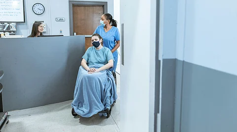 A nurse assisting a patient in a wheelchair in a hospital corridor.