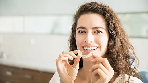 Portrait of beautiful patient holding orthodontic retainers in dental clinic.