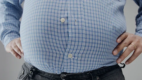 A man resting his hands on both sides of his waist, conveying his sense of worry on expanding waistline.