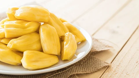 A white plate holds a pile of ripe yellow jackfruit, showcasing its unique texture and vibrant color.