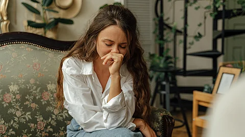 A woman is sitting on floral designed sofa wearing a white shirt and light blue pants.